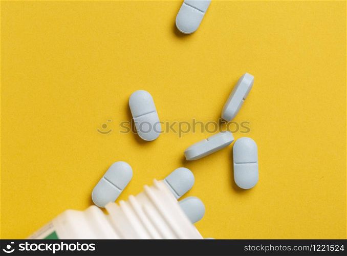 Medicine bottle and blue drugs scattered around on yellow background. Medicine bottle and blue pills scattered around on yellow background
