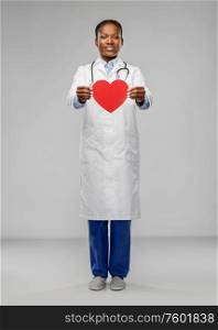 medicine, cardioligy and healthcare concept - smiling african american female doctor in white coat with red heart and stethoscope over grey background. african american female doctor with red heart