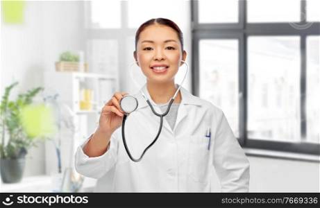 medicine, cardiology and healthcare concept - close up of happy smiling asian female doctor in white coat with stethoscope over medical office at hospital on background. close up of asian female doctor with stethoscope