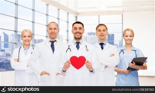 medicine, cardiology, healthcare and people concept - happy young doctors cardiologists with red heart over clinic background