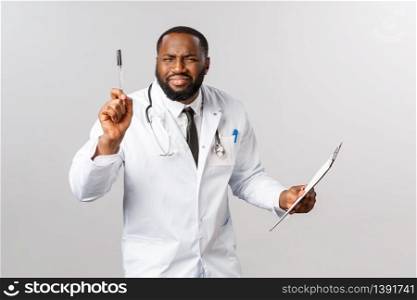 Medicine, covid19, treatment and hospital concept. Funny african-american doctor in white coat, holding clipboard and pen, squinting trying to write down patient info, tell uncomfortable news.. Medicine, covid19, treatment and hospital concept. Funny african-american doctor in white coat, holding clipboard and pen, squinting trying to write down patient info, tell uncomfortable news
