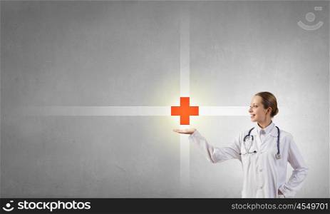 Medicine cross symbol. Attractive female doctor in white showing medicine cross sign
