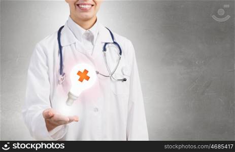 Medicine cross symbol. Female doctor in white showing light bulb with medicine cross sign