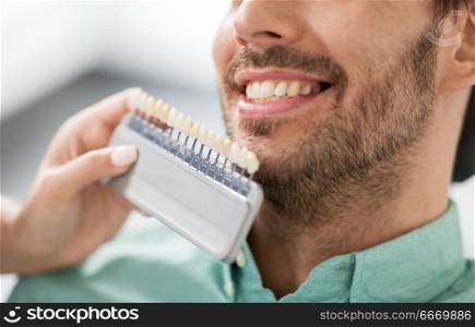 medicine, dentistry and healthcare concept - close up of dentist with tooth color samples choosing shade for male patient teeth at dental clinic. dentist choosing tooth color for patient at clinic. dentist choosing tooth color for patient at clinic