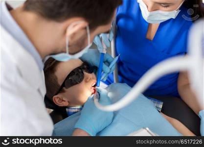medicine, dentistry and healthcare concept - dentist and assistant with dental drill and saliva ejector treating kid patient teeth at dental clinic. dentist treating kid teeth at dental clinic. dentist treating kid teeth at dental clinic