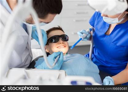 medicine, dentistry and healthcare concept - dentist and assistant with dental drill and saliva ejector treating kid patient teeth at dental clinic. dentist treating kid teeth at dental clinic. dentist treating kid teeth at dental clinic