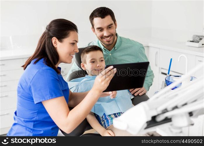 medicine, dentistry and healthcare concept - dentist showing tablet pc computer to kid patient and his father at dental clinic. dentist showing tablet pc to kid at dental clinic. dentist showing tablet pc to kid at dental clinic