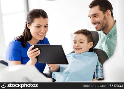 medicine, dentistry and healthcare concept - dentist showing tablet pc computer to kid patient and his father at dental clinic. dentist showing tablet pc to kid at dental clinic. dentist showing tablet pc to kid at dental clinic