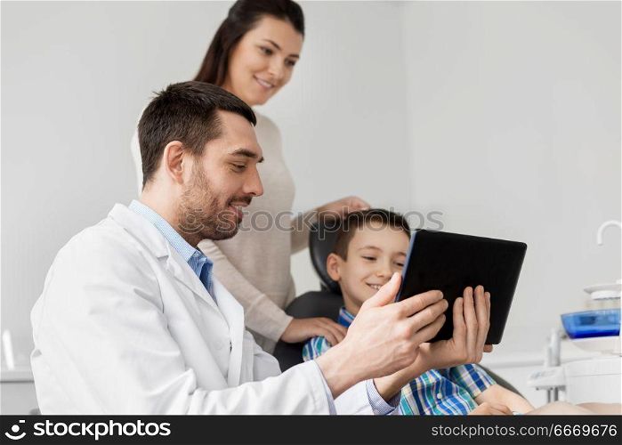 medicine, dentistry and healthcare concept - dentist showing tablet pc computer to kid patient and his mother at dental clinic. dentist showing tablet pc to kid at dental clinic. dentist showing tablet pc to kid at dental clinic