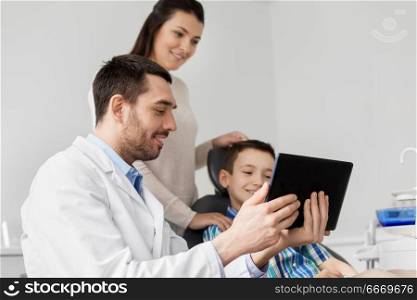 medicine, dentistry and healthcare concept - dentist showing tablet pc computer to kid patient and his mother at dental clinic. dentist showing tablet pc to kid at dental clinic. dentist showing tablet pc to kid at dental clinic