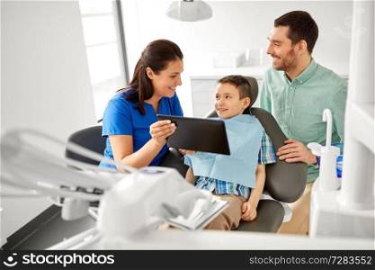 medicine, dentistry and healthcare concept - dentist showing tablet pc computer to kid patient and his father at dental clinic. dentist showing tablet pc to kid at dental clinic