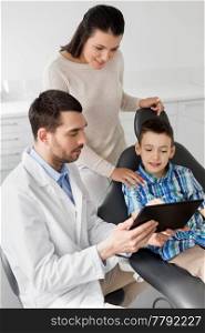 medicine, dentistry and healthcare concept - dentist showing tablet pc computer to kid patient and his mother at dental clinic. dentist showing tablet pc to kid at dental clinic