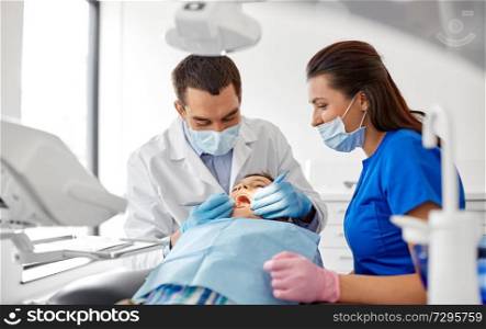 medicine, dentistry and healthcare concept - dentist with mouth mirror and probe checking for kid patient teeth at dental clinic. dentist checking for kid teeth at dental clinic
