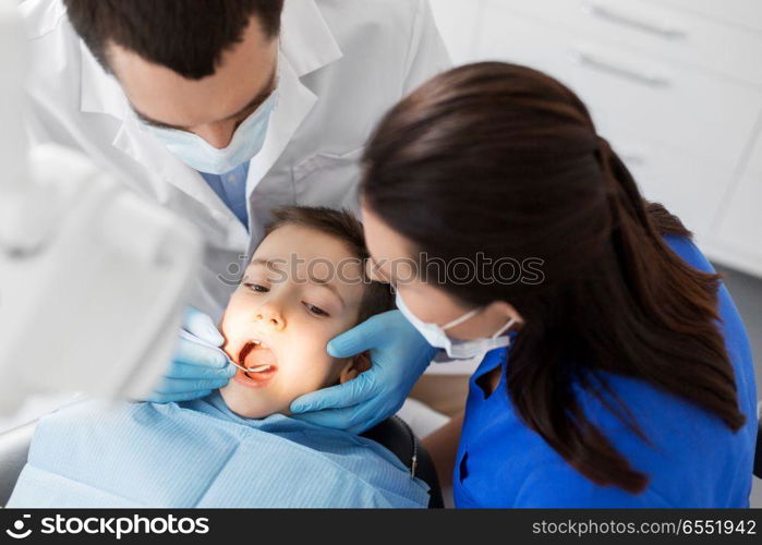 medicine, dentistry and healthcare concept - dentist with mouth mirror checking for kid patient teeth at dental clinic. dentist checking for kid teeth at dental clinic. dentist checking for kid teeth at dental clinic