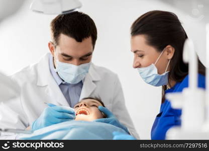 medicine, dentistry and healthcare concept - dentist with mouth mirror checking for kid patient teeth at dental clinic. dentist checking for kid teeth at dental clinic