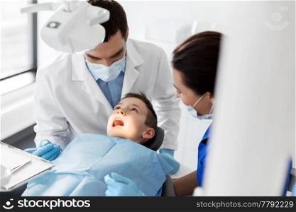medicine, dentistry and healthcare concept - dentist with mouth mirror checking for kid patient teeth at dental clinic. dentist checking for kid teeth at dental clinic