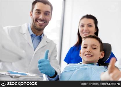medicine, dentistry and healthcare concept - dentists and happy kid patient at dental clinic showing thumbs up. dentists and happy kid patient at dental clinic. dentists and happy kid patient at dental clinic