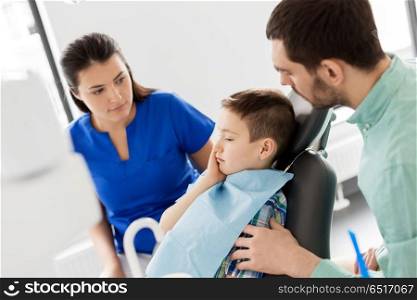 medicine, dentistry and healthcare concept - father and son suffering from toothache visiting dentist at dental clinic. father and son visiting dentist at dental clinic. father and son visiting dentist at dental clinic