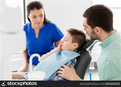 medicine, dentistry and healthcare concept - father and son suffering from toothache visiting dentist at dental clinic. father and son visiting dentist at dental clinic. father and son visiting dentist at dental clinic