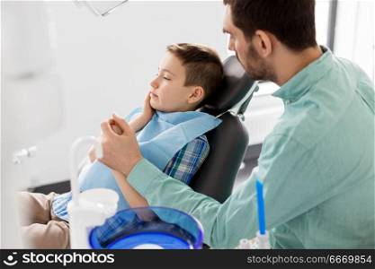 medicine, dentistry and healthcare concept - father supporting son suffering from toothache at dental clinic. father supporting son at dental clinic. father supporting son at dental clinic