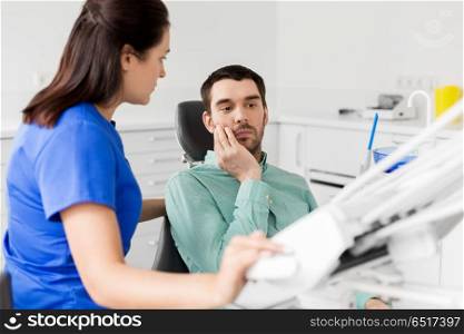 medicine, dentistry and healthcare concept - female dentist talking to male patient complaining of toothache at dental clinic office. patient with toothache at dentist office. patient with toothache at dentist office