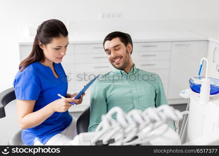 medicine, dentistry and healthcare concept - female dentist with clipboard and male patient at dental clinic office. dentist and patient discussing dental treatment. dentist and patient discussing dental treatment