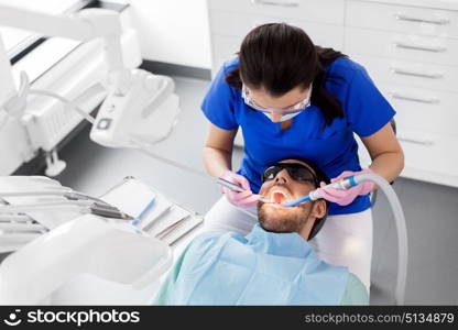 medicine, dentistry and healthcare concept - female dentist with drill and saliva ejector treating male patient teeth at dental clinic. dentist treating patient teeth at dental clinic. dentist treating patient teeth at dental clinic