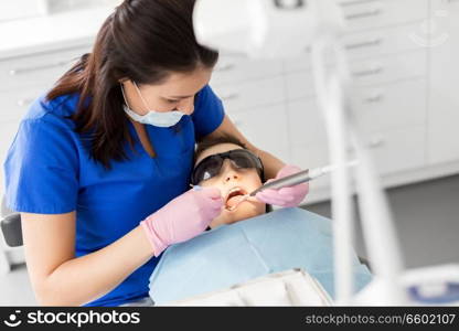 medicine, dentistry and healthcare concept - female dentist with mouth mirror and water gun checking for kid patient teeth at dental clinic. dentist checking for kid teeth at dental clinic