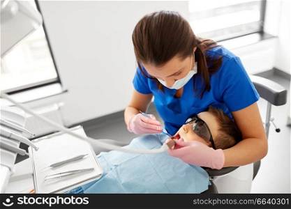 medicine, dentistry and healthcare concept - female dentist with mouth mirror and water gun checking for kid patient teeth at dental clinic. dentist checking for kid teeth at dental clinic
