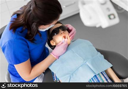 medicine, dentistry and healthcare concept - female dentist with mouth mirror checking for kid patient teeth at dental clinic. dentist checking for kid teeth at dental clinic. dentist checking for kid teeth at dental clinic