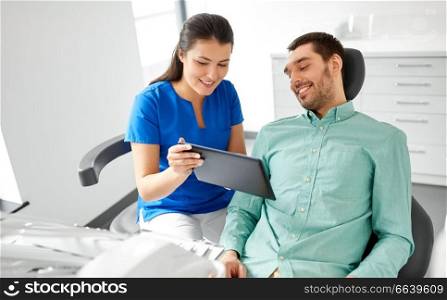 medicine, dentistry and healthcare concept - female dentist with tablet pc computer and male patient discussing teeth treatment at dental clinic office. dentist and patient with tablet pc at clinic
