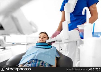medicine, dentistry and healthcare concept - female dentist with x-ray machine scanning kid patient teeth at dental clinic. dentist making x-ray of kid teeth at dental clinic