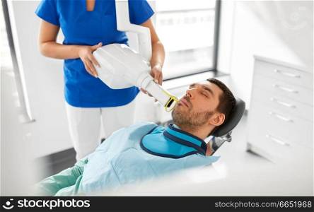 medicine, dentistry and healthcare concept - female dentist with x-ray machine scanning male patient teeth at dental clinic. dentist making dental x-ray of patient teeth