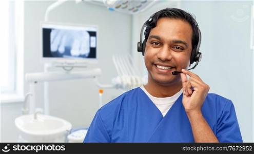 medicine, dentistry and healthcare concept - happy smiling indian doctor or male dentist with headset over dental clinic background. smiling indian doctor or male nurse with headset