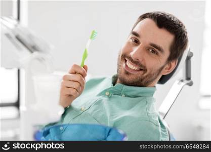 medicine, dentistry and healthcare concept - happy smiling male patient with toothbrush on chair at dental clinic. smiling man with toothbrush at dental clinic. smiling man with toothbrush at dental clinic