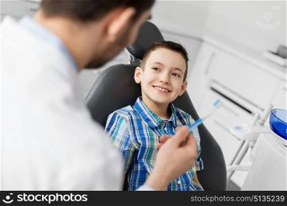 medicine, dentistry and healthcare concept - male dentist giving toothbrush to kid patient at dental clinic. dentist giving toothbrush to kid patient at clinic. dentist giving toothbrush to kid patient at clinic
