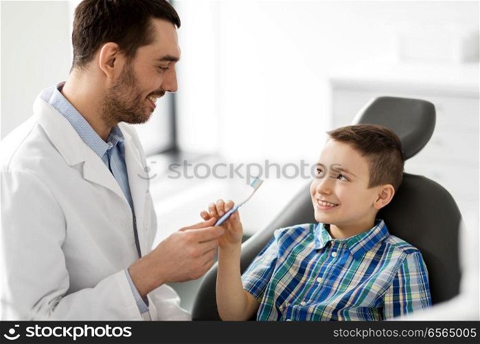 medicine, dentistry and healthcare concept - male dentist giving toothbrush to kid patient at dental clinic. dentist giving toothbrush to kid patient at clinic