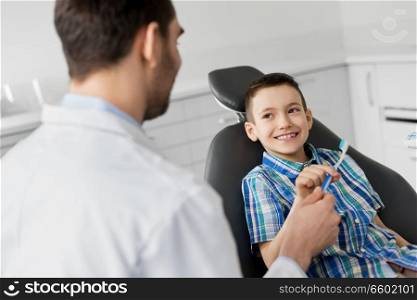 medicine, dentistry and healthcare concept - male dentist giving toothbrush to kid patient at dental clinic. dentist giving toothbrush to kid patient at clinic