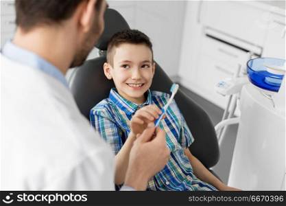 medicine, dentistry and healthcare concept - male dentist giving toothbrush to kid patient at dental clinic. dentist giving toothbrush to kid patient at clinic. dentist giving toothbrush to kid patient at clinic