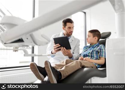 medicine, dentistry and healthcare concept - male dentist showing tablet pc computer to kid patient at dental clinic. dentist showing tablet pc to kid patient at clinic. dentist showing tablet pc to kid patient at clinic