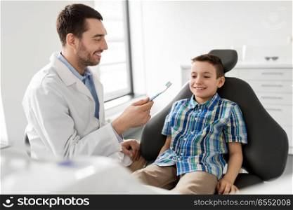 medicine, dentistry and healthcare concept - male dentist showing toothbrush to kid patient at dental clinic. dentist with toothbrush and kid patient at clinic. dentist with toothbrush and kid patient at clinic