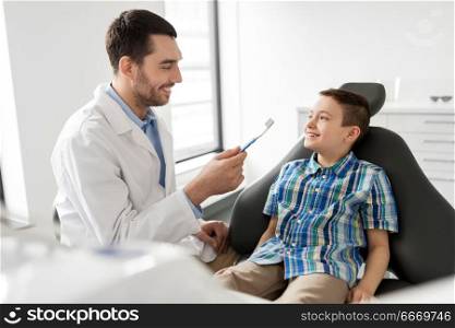 medicine, dentistry and healthcare concept - male dentist showing toothbrush to kid patient at dental clinic. dentist with toothbrush and kid patient at clinic. dentist with toothbrush and kid patient at clinic