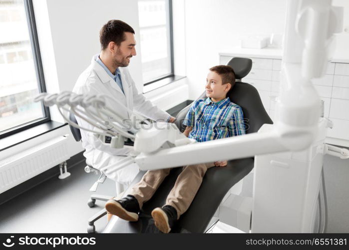 medicine, dentistry and healthcare concept - male dentist talking to kid patient at dental clinic. dentist talking to kid patient at dental clinic. dentist talking to kid patient at dental clinic