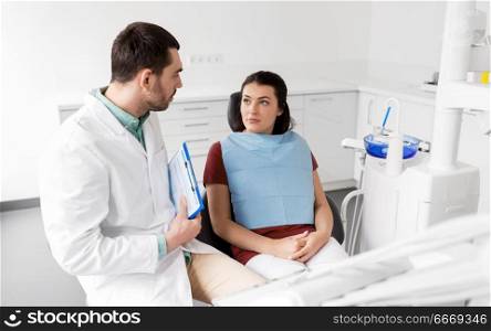 medicine, dentistry and healthcare concept - male dentist with clipboard talking to female patient and discussing teeth treatment at dental clinic office. dentist talking to female patient at dental clinic. dentist talking to female patient at dental clinic
