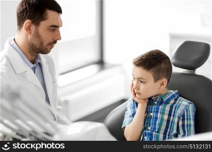 medicine, dentistry and healthcare concept - male dentist with kid patient suffering from toothache at dental clinic adjusting chair. dentist with patient having toothache at clinic. dentist with patient having toothache at clinic