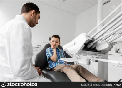 medicine, dentistry and healthcare concept - male dentist with kid patient suffering from toothache at dental clinic adjusting chair. dentist with patient having toothache at clinic. dentist with patient having toothache at clinic