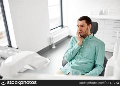 medicine, dentistry and healthcare concept - male patient suffering from toothache at dental clinic office. patient suffering from toothache at dental clinic