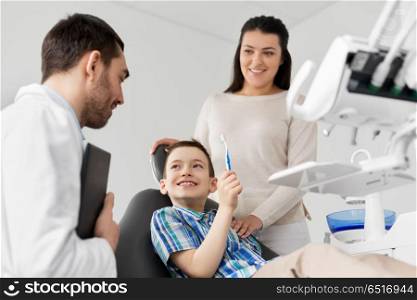 medicine, dentistry and healthcare concept - mother and son with toothbrush visiting dentist at dental clinic. mother and son visiting dentist at dental clinic. mother and son visiting dentist at dental clinic