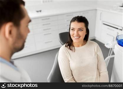 medicine, dentistry and healthcare concept - smiling female patient talking to dentist at dental clinic office. female patient talking to dentist at dental clinic. female patient talking to dentist at dental clinic