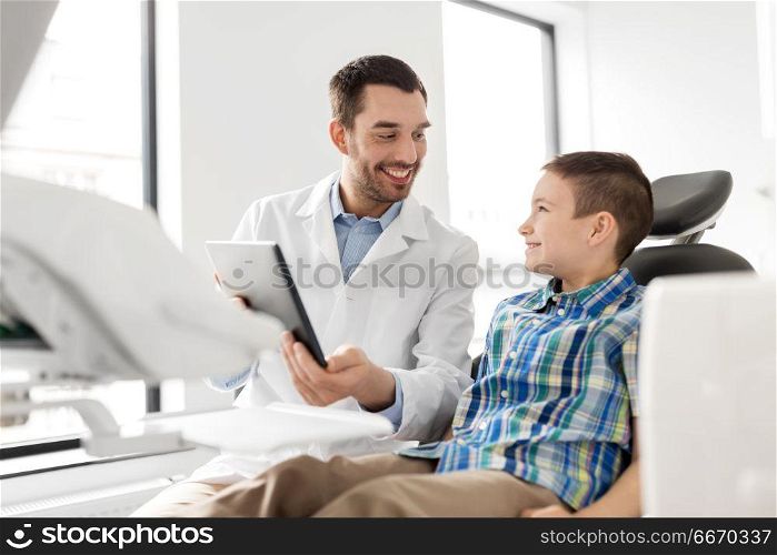 medicine, dentistry and healthcare concept - smiling male dentist showing tablet pc computer to kid patient at dental clinic. dentist showing tablet pc to kid patient at clinic. dentist showing tablet pc to kid patient at clinic